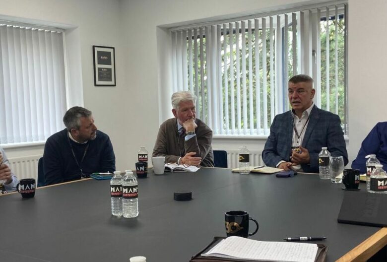 Many people sat around a table discussing collaborative marketing. The table is cluttered with papers and mugs.
