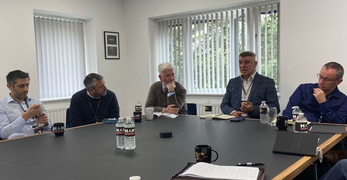 Many people sat around a table discussing collaborative marketing. The table is cluttered with papers and mugs.